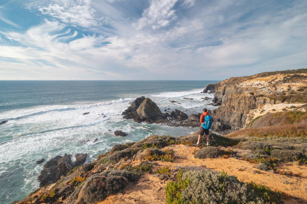 istock Joyful expression of a young backpacker standing on the edge of a cliff overlooking the Atlantic Ocean in the Odemira region, western Portugal. Wandering along the Fisherman Trail, Rota Vicentina 1488334755
