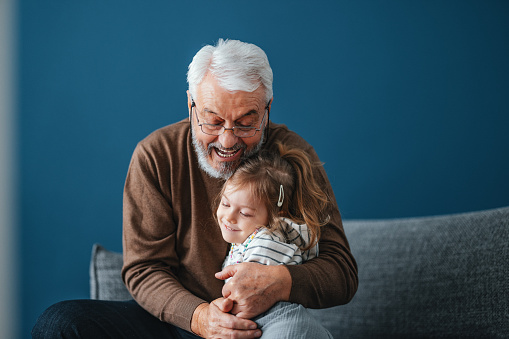 Portrait of cheerful grandpa being affectionate with his granddaughter. He is smiling and embracing her in a hug. They are enjoying spending time together.