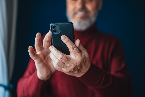 Low angle view of an anonymous mature man typing text message on his smartphone while standing in the living room.