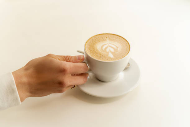 istock Female hand holding white cup with fresh coffee on white table 1488336433