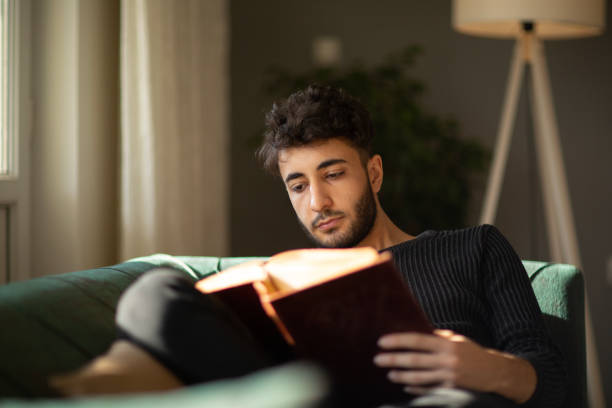 istock Young man relaxing with a book on his sofa at hom 1488339516