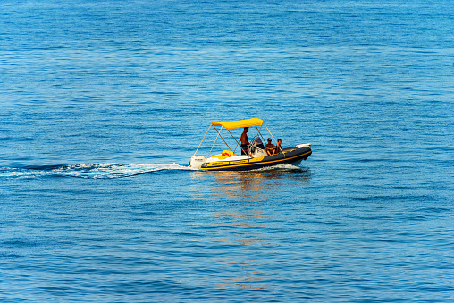 La Spezia, Italy - July 20, 2022: Small black and orange motorized dinghy with a family on board (a man, a woman and a boy), on a sunny summer day in the blue Mediterranean sea, Tellaro, Lerici municipality, Gulf of La Spezia or Gulf of Poets, Liguria, Italy, southern Europe.