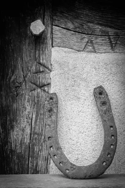 An old horseshoe stands against a wall of wood and stone, vertical, black and white