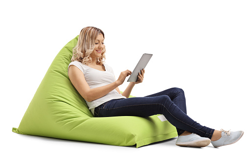 Young woman on a bean bag chair using a digital tablet isolated on white background