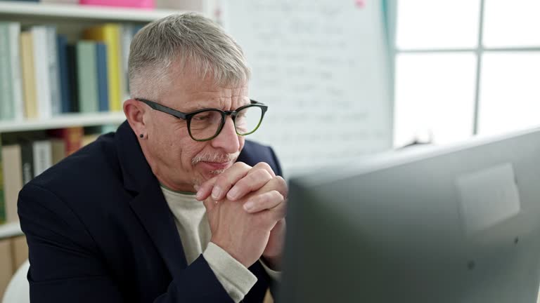 Middle age grey-haired man teacher using computer thinking at university classroom