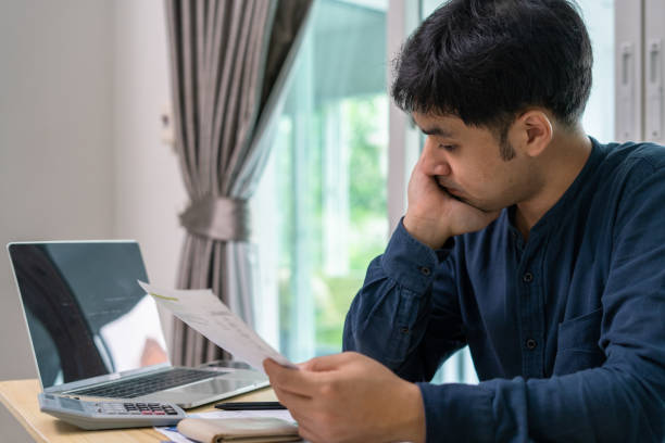 männer stressen sich über viele kreditkartenschulden und rechnungen auf dem boden. die hausfrau hat schwierigkeiten, die monatlichen ausgaben zu berechnen, und das budget reicht nicht aus, um die schulden zu begleichen - asian ethnicity surprise men shock stock-fotos und bilder