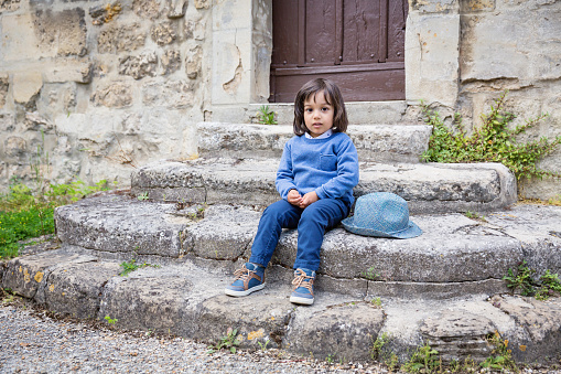 Little handsome baby boy sitting on ancient stone stairs outdoor in old city