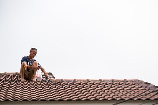 Phayao, Thailand, May,3,2023: roofing contractor Seal the roof leaks with  sealant in the rainy season, on the backdrop of the sky in the rainy season