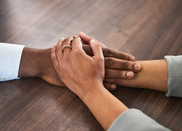 istock Support, help and couple holding hands for trust, empathy and unity in crisis, cancer or bad news. Solidarity, care and man and woman together on table for praying, comfort and prayer, hope or love. 1488356110
