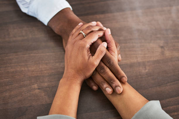 istock Holding hands, support and trust with people, closeup on wood table with communication, relationship and solidarity. Wellness, mental health or praying with counselling or worship, help and comfort 1488356129