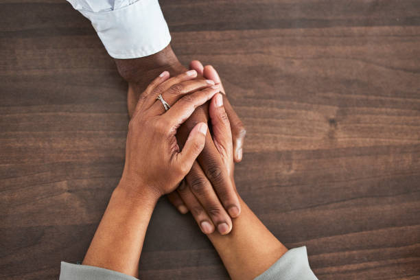 istock Holding hands, support and trust with people, help and closeup on wood table with communication and relationship. Above, mental health or praying with counselling or worship, solidarity and empathy 1488356132