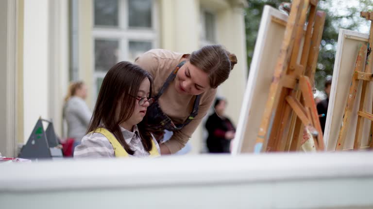 The girl with a mental disability drawing a picture with a caregiver during the art therapy outdoors on the terrasse