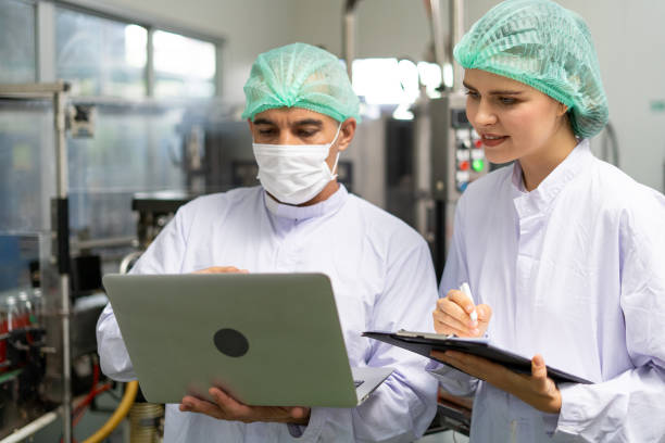 istock Quality control engineer holds computer to work with female worker. Workers in the factory write down notes about bottles or gallons before send to customers. Inspection quality control. 1488358047
