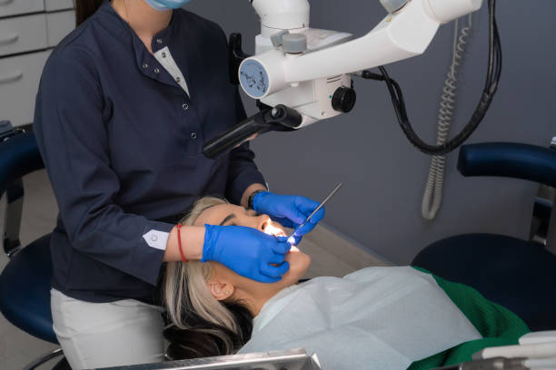 istock Female dentist using dental microscope treating patient teeth dental clinic office. undergoing treatment by experienced dentist using microscope. Image of woman on patient's chair in dentist's office. 1488358807