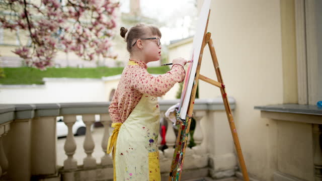A portrait of the girl with psychological disabilities draws a picture outside under the spring bloosom