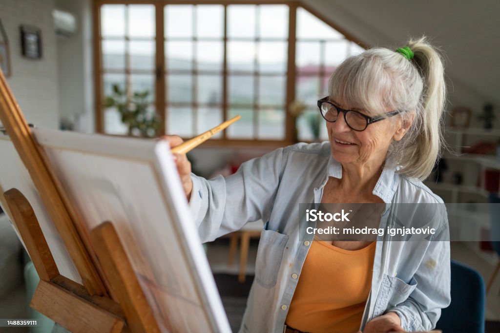 Senior woman painting on a canvas in her apartment's living room Senior Caucasian woman painting on a canvas in her apartment's living room 70-79 Years Stock Photo
