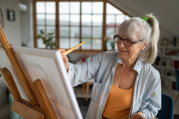 Senior woman painting on a canvas in her apartment's living room Senior Caucasian woman painting on a canvas in her apartment's living room painted image paintings oil paint senior women stock pictures, royalty-free photos & images