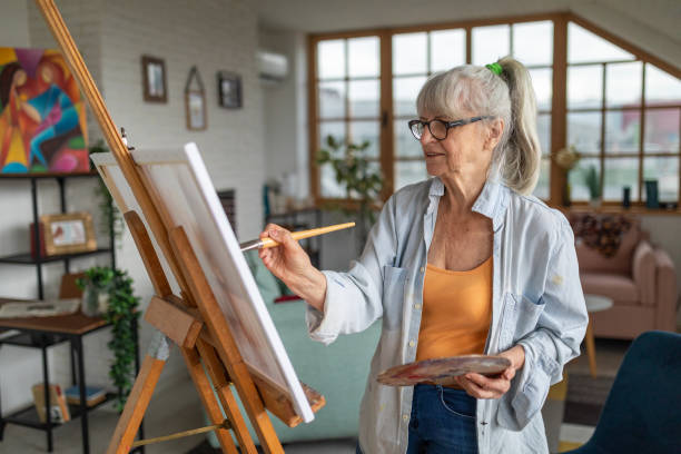 Senior woman painting on a canvas in her apartment's living room Senior Caucasian woman painting on a canvas in her apartment's living room painted image paintings oil paint senior women stock pictures, royalty-free photos & images