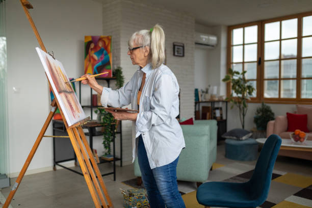 Senior woman painting on a canvas in her apartment's living room Senior Caucasian woman painting on a canvas in her apartment's living room painted image paintings oil paint senior women stock pictures, royalty-free photos & images