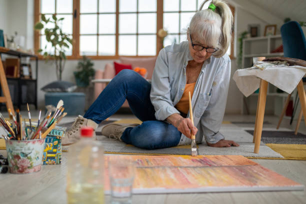 Senior woman sitting on the floor and painting on a canvas Senior Caucasian woman sitting on the floor and painting on a canvas painted image paintings oil paint senior women stock pictures, royalty-free photos & images