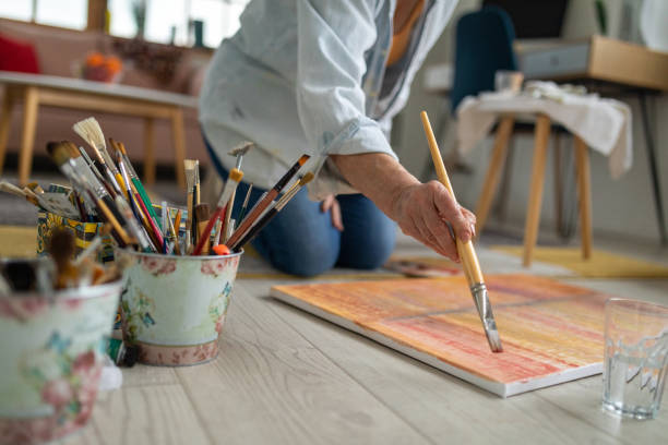 Senior woman sitting on the floor and painting on a canvas Senior Caucasian woman sitting on the floor and painting on a canvas painted image paintings oil paint senior women stock pictures, royalty-free photos & images