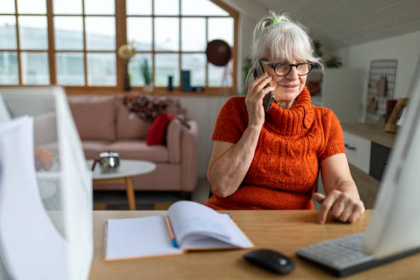 istock Senior woman using a computer and talking on her smart phone at home 1488361414