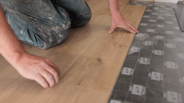 Renovation, construction, flooring and people concept - close-up of a man installing a wooden floor.