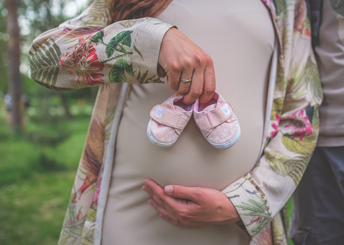 Pregnant woman holding her stomach and small baby shoes outside