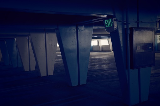 A dark parking garage, featuring a lit exit sign on the column