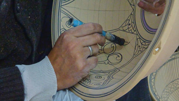 craftsman painting ornamental design onto a ceramic pottery.