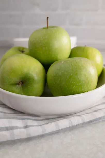 Fresh green apples with water drops  in a white bowl islated on kitchen table background. Closeup, front view