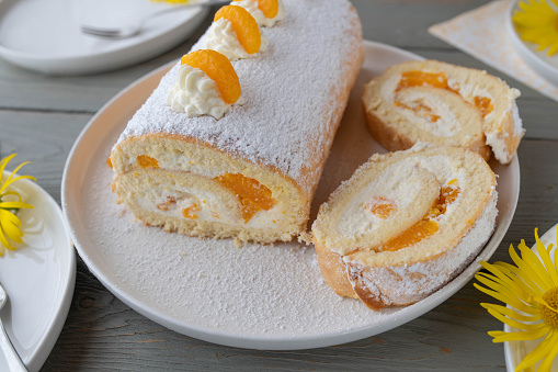 Homemade traditional swiss roll with cream and mandarin orange filling. Served ready to eat  with plates on a table.