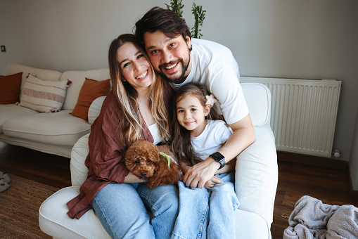 Portrait of happy family embracing daughter and dog while sitting on couch in cozy home interior against green wall, copy space