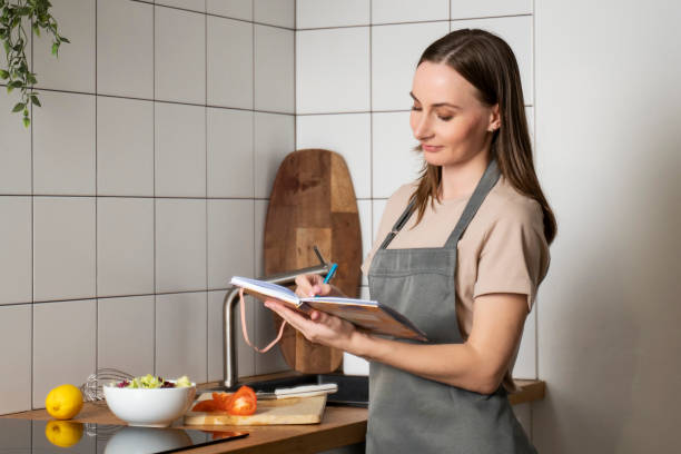 istock A smiling young beautiful business woman makes notes in a paper diary in a modern kitchen. A happy woman writing in a notebook surrounded by a convenient storage organization 1488373659