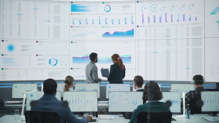 Wide Zoom Out Back Shot Of Diverse Male And Female Risk Managers Analyzing Data On Digital Screen In Monitoring Room. Multiethnic Employees Working On Computers For Succesful Consulting Company