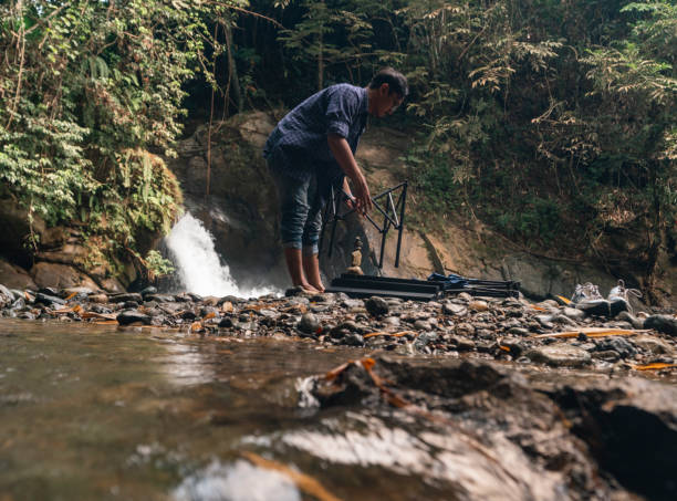istock an asian man preparing his folding chairs and table for relaxing in the front of a small waterfall in a tropical rainforest 1488377492