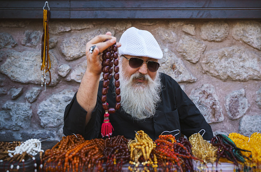Senior man with a long white beard sells muslim prayer beads (tasbih) on the street, Ankara, Turkiye