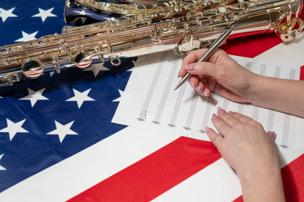 nahaufnahme von weiblichen händen, die noten auf ein notenblatt schreiben, vor dem hintergrund der amerikanischen flagge - close up musical instrument saxophone jazz stock-fotos und bilder