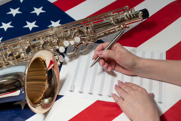 nahaufnahme von weiblichen händen, die noten auf ein notenblatt schreiben, vor dem hintergrund der amerikanischen flagge - close up musical instrument saxophone jazz stock-fotos und bilder