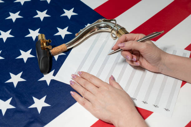 nahaufnahme von weiblichen händen, die noten auf ein notenblatt schreiben, vor dem hintergrund der amerikanischen flagge - close up musical instrument saxophone jazz stock-fotos und bilder