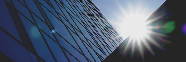 corporate city building with panoramic windows on wall silhouette lit by bright sun under blue sky on summer day