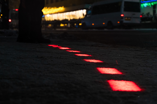 Pedestrian crossing, the red signal of the ground traffic light on a winter evening during a snowfall. New modern ground traffic lights built on the sidewalk for pedestrians