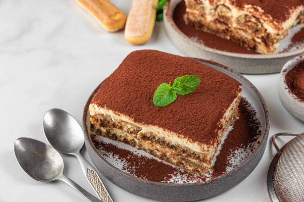 伝統的なイタリアのデザートティラミスを皿に。新鮮なミントとスプーンを使った自家製ティラミスケーキの部分 - tiramisu cake chocolate sweet food ストックフォトと画像