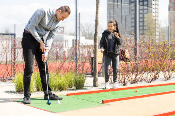 istock Sharing with golf experience. Cheerful young man teaching his daughter to play mini golf at the day time. Concept of friendly family 1488391247
