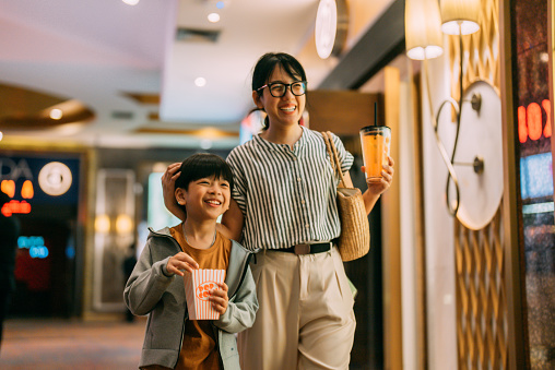 Asian  mother and her son buying popcorn from cinema bar counter.Asian bartender serving  in front bar counter for popcorn before movie show time .