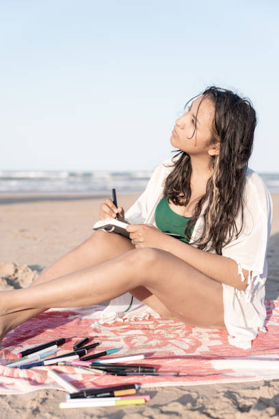 istock A young Hispanic woman is looking at the sky while drawing on the beach in her notebook 1488394577