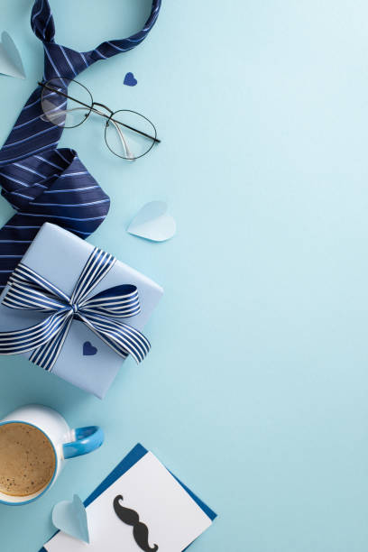 istock Classy Father's Day concept. Top view flat lay of envelope with card, gift box, necktie, accessories, hearts, spectacles, coffee cup on blue background with space for message or advert 1488394674