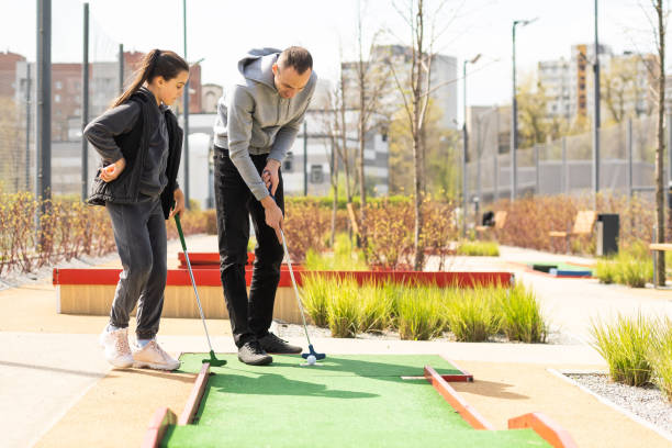 istock Sharing with golf experience. Cheerful young man teaching his daughter to play mini golf at the day time. Concept of friendly family 1488395625