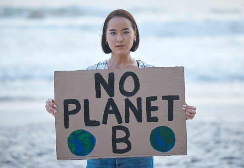 Protest, planet earth and woman with a sign on beach to stop pollution, climate change and global warming. Political, earth activism and portrait of Asian female leader with board by ocean for march.