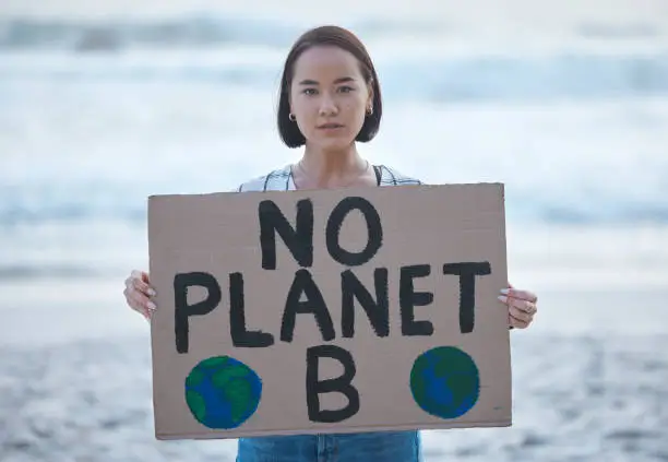 Photo of Protest, planet earth and woman with a sign for climate change to stop pollution and global warming at beach. Political, nature activism and portrait of Asian female with board by ocean for march